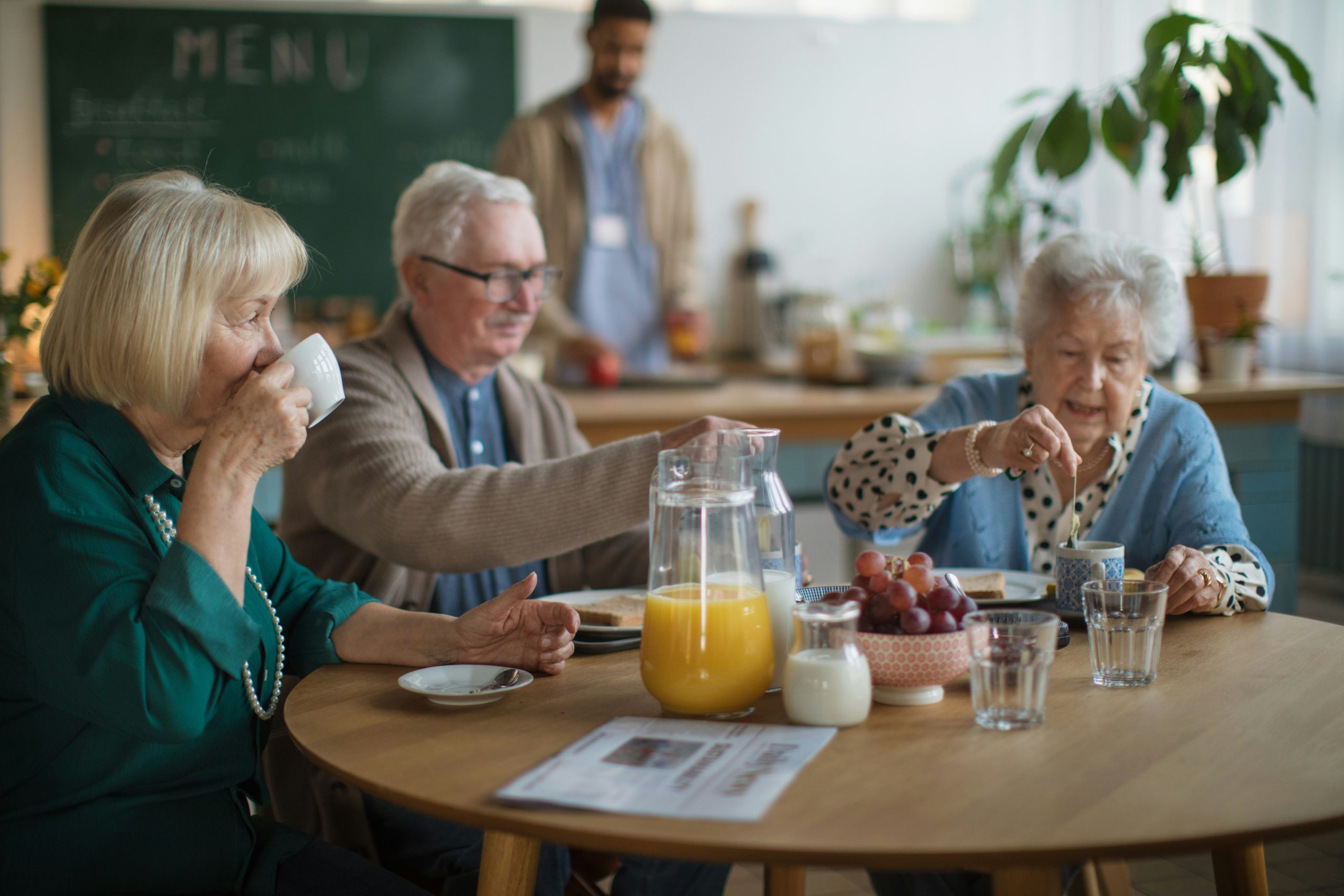 a group of seniors sitting around a dining table with orange juice and fruits