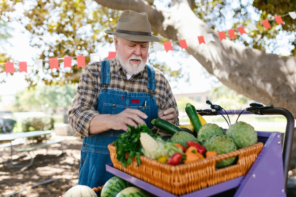 A senior stands outside at a farmers market with a basket of vegetables