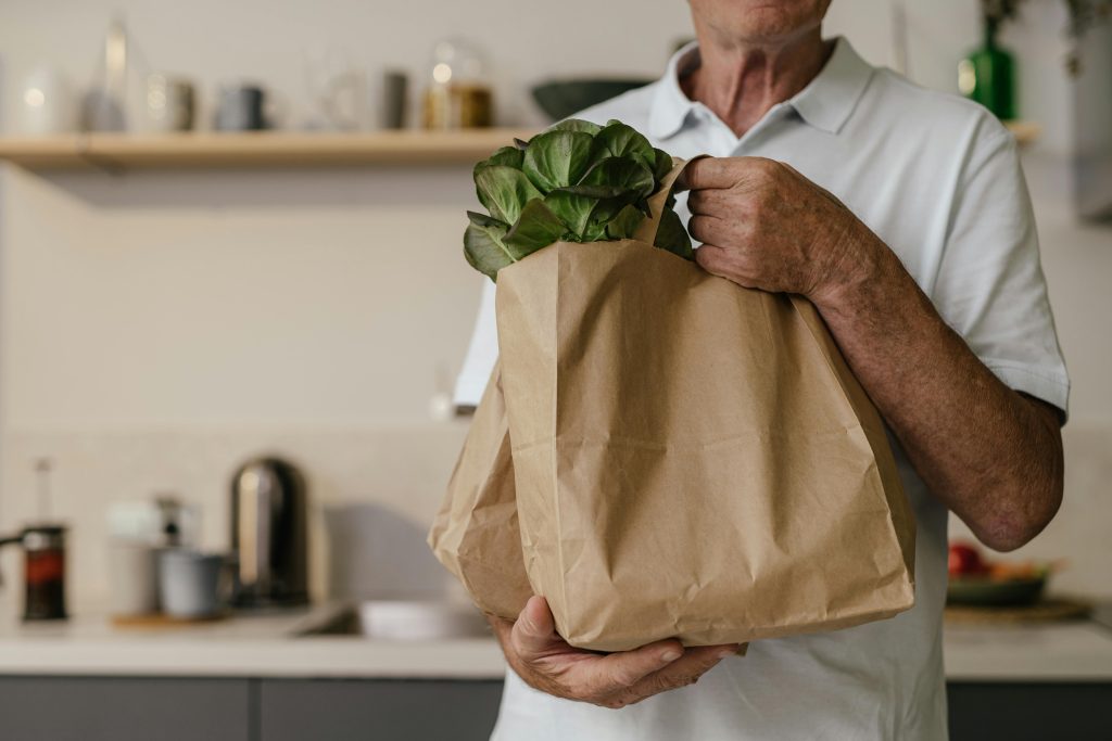 a man stands in a kitchen holding a brown paper bag of vegetables